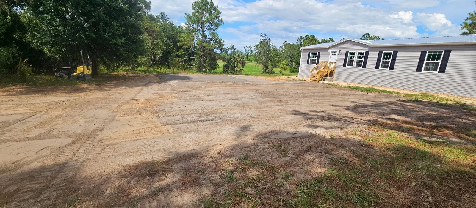 Loose graded sand and track marks in front of the home, with the roller parked at the edge