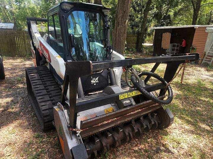 A Bobcat T76 track loader with the forestry mulching head mounted, drum and carbide teeth visible